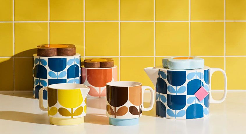 Orla Kiely teapot and mugs on a white counter with yellow tiles behind. 